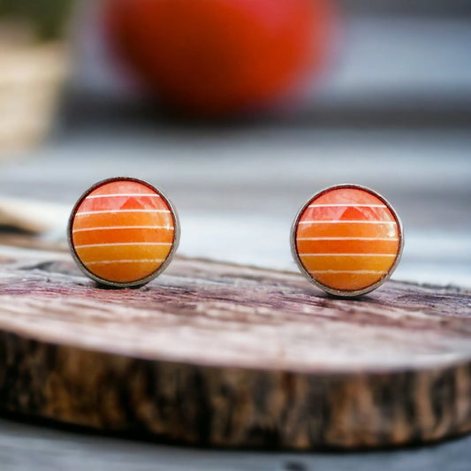 Round orange gradient striped stud earrings in a silver-tone setting displayed on a rustic wood surface