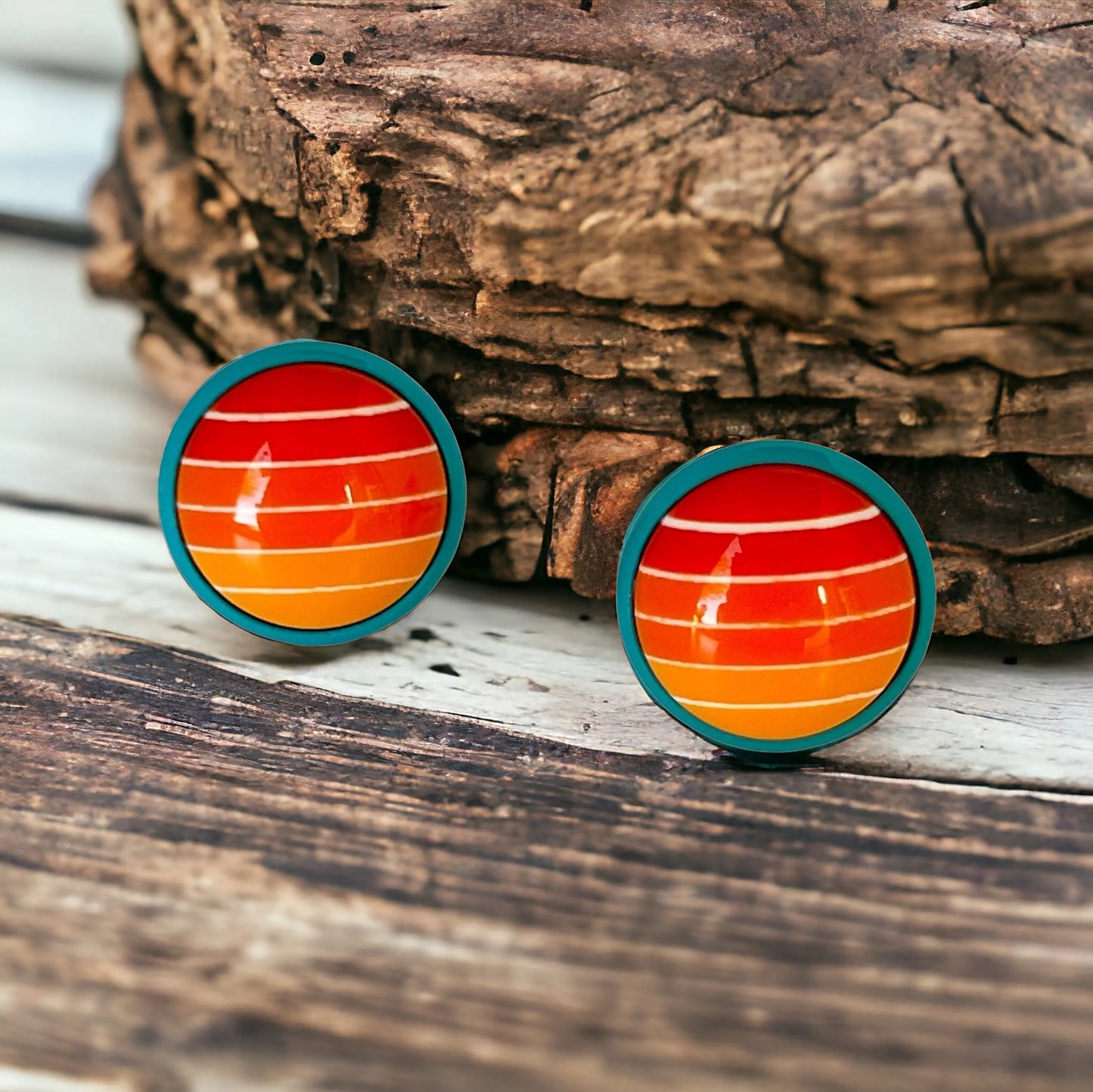 Round orange gradient striped stud earrings with teal borders displayed on a light wood background