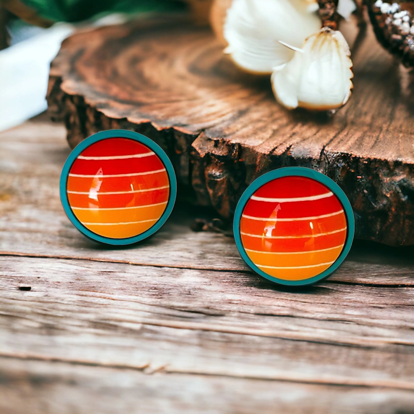 Round orange gradient striped stud earrings with teal borders displayed on a light wood boho background
