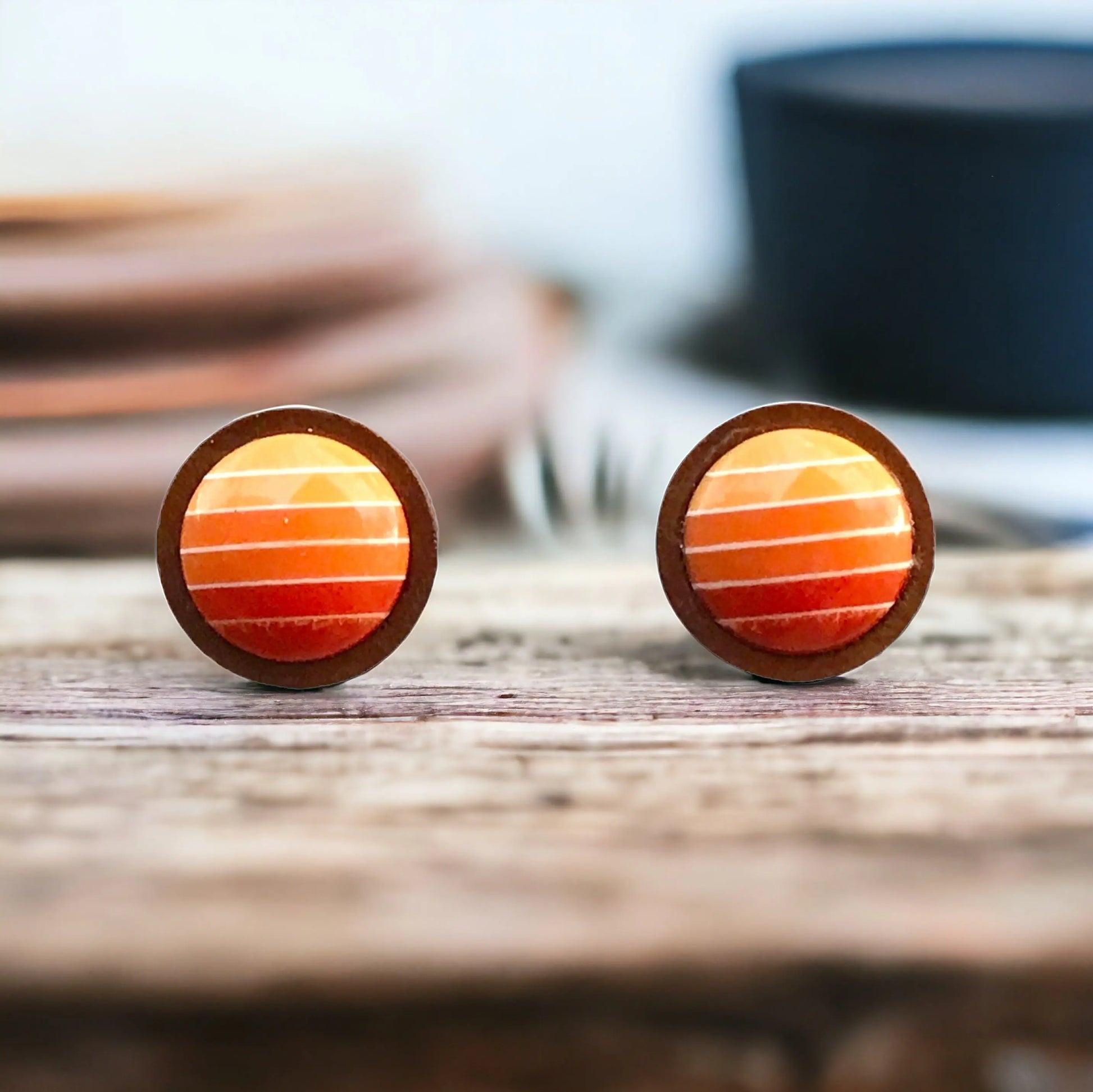 Round orange gradient striped wood stud earrings displayed on a rustic wood surface