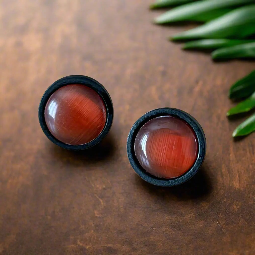 Round orange resin stud earrings with black wood borders displayed on a dark wood surface