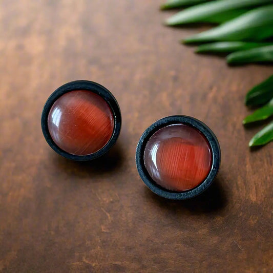 Round orange resin stud earrings with black wood borders displayed on a dark wood surface