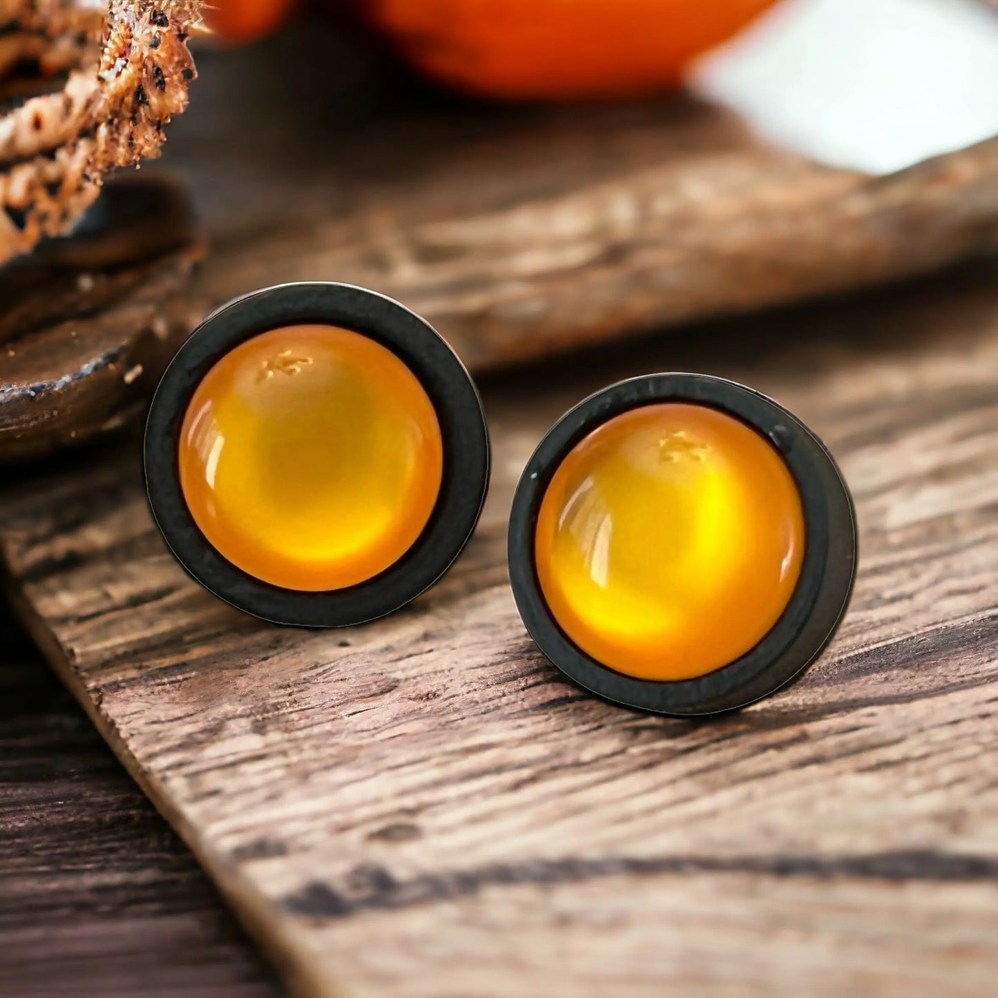 Pair of earrings with orange centers on a boho wooden surface
