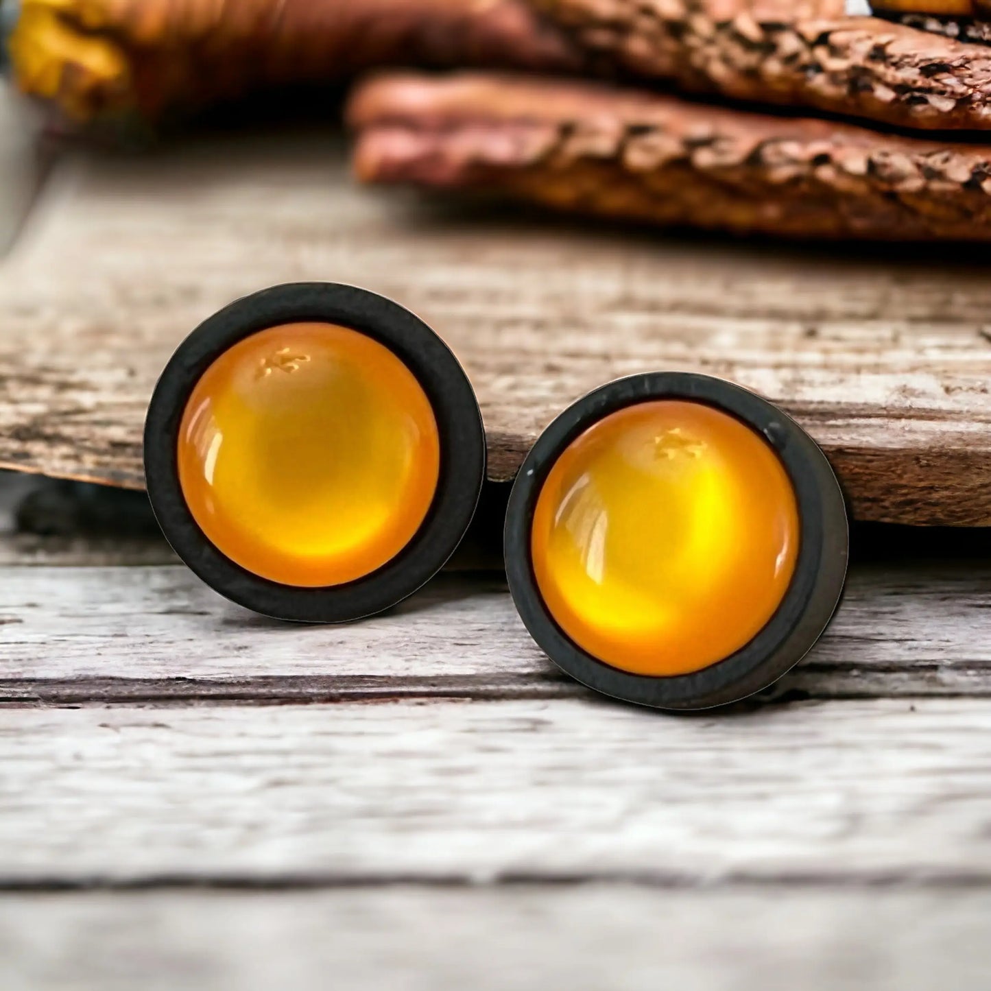 Two round orange earrings with black rims on a whitewashed wooden surface