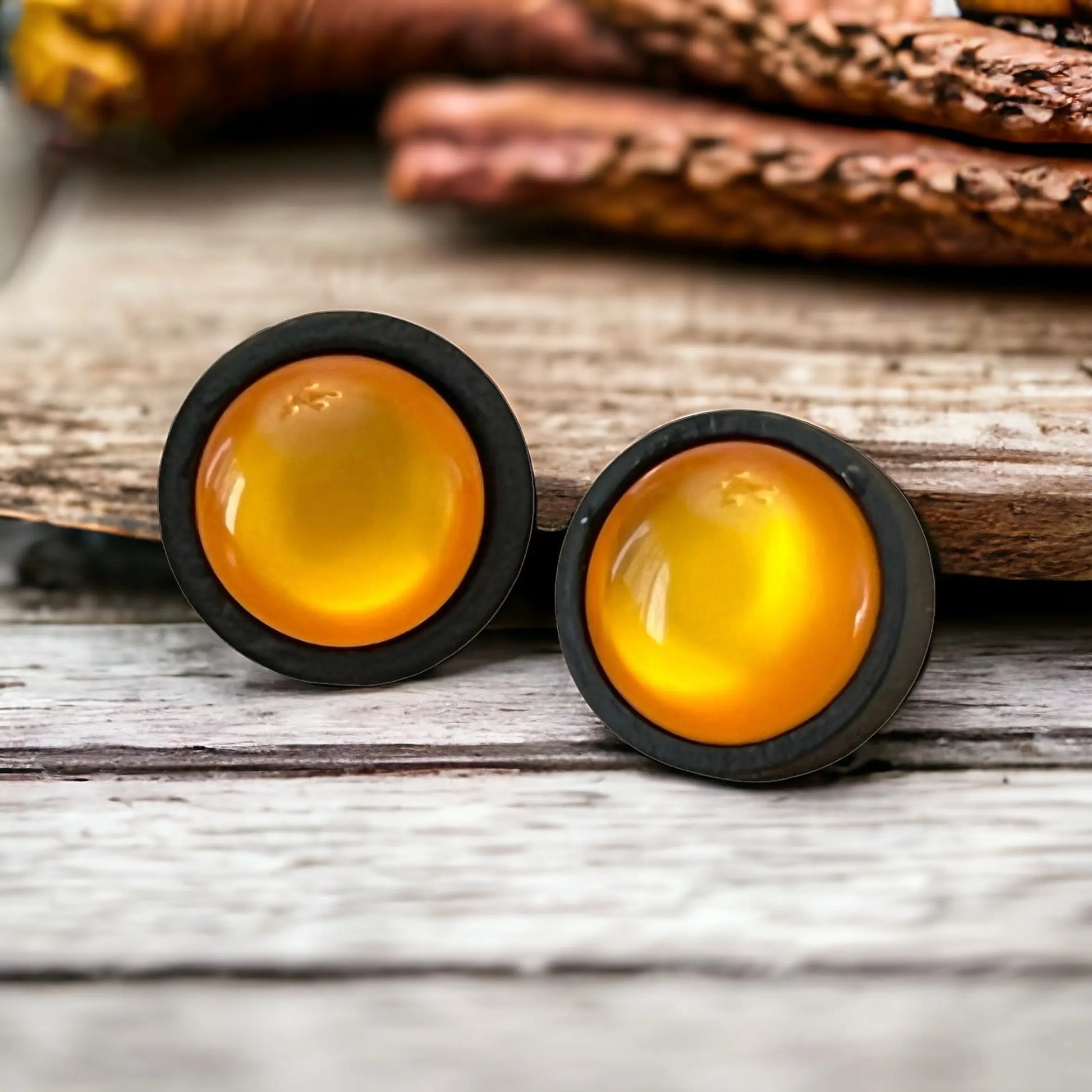 Two round orange earrings with black rims on a whitewashed wooden surface