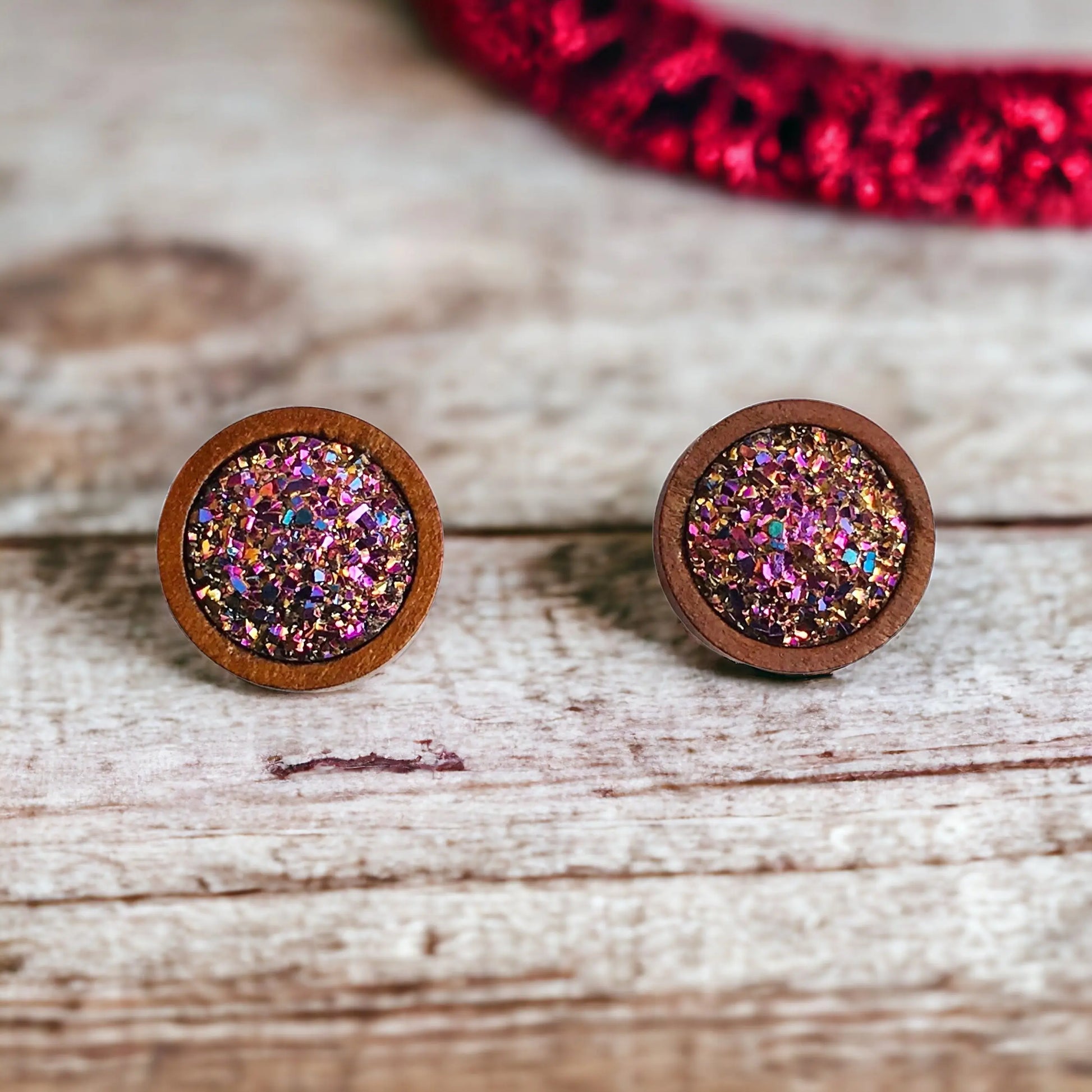 Round pink glitter druzy wood stud earrings displayed on a rustic white wood surface