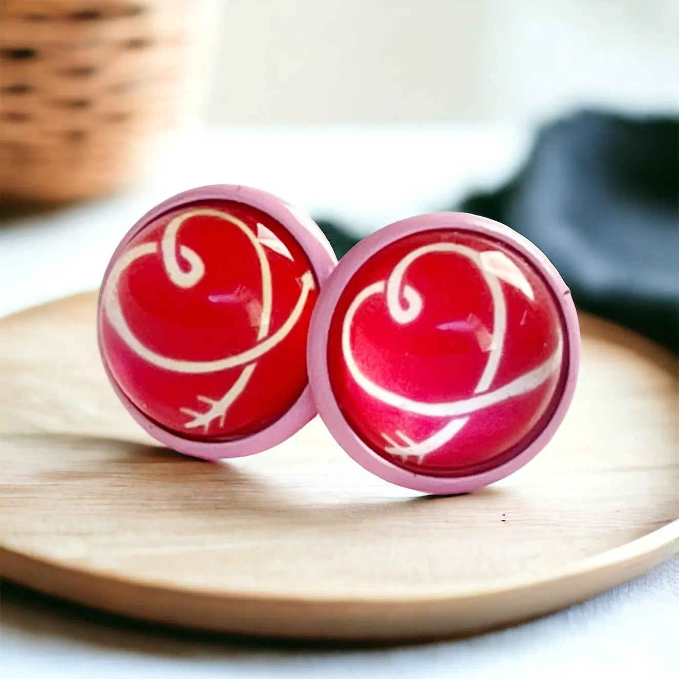 A pair of pink earrings with a red background and white hearts on a wooden plate