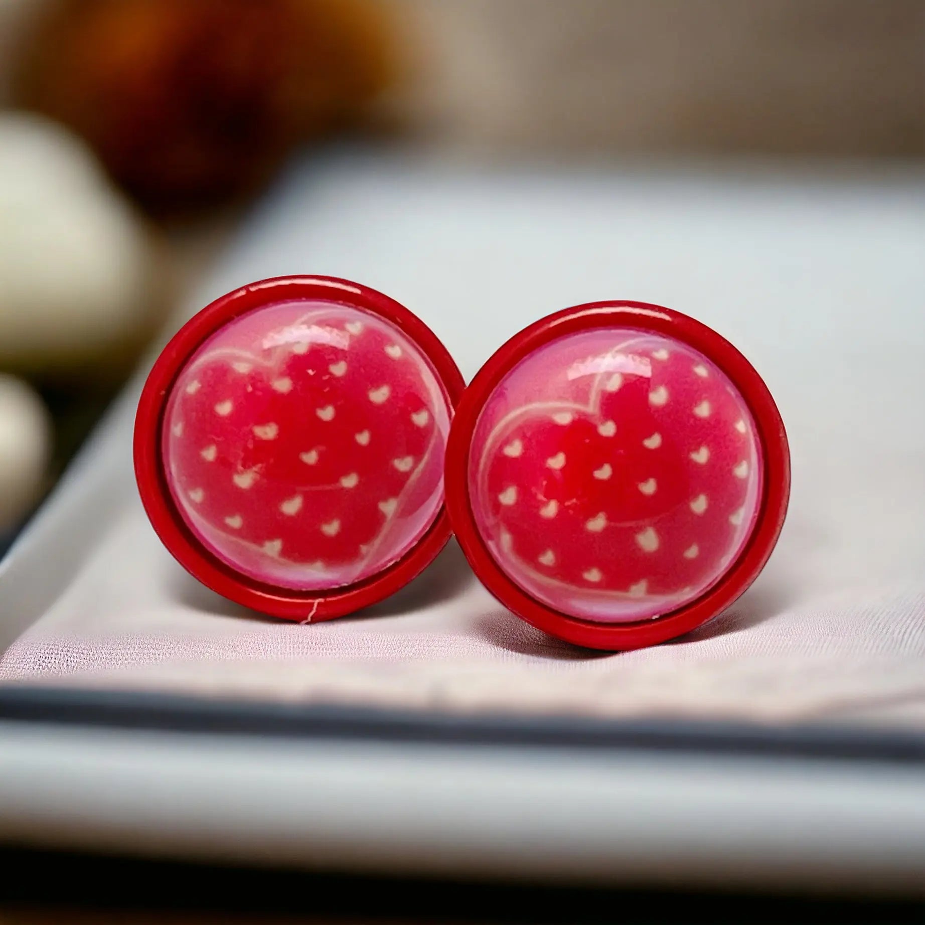 Pair of red earrings with white heart design on a neutral background