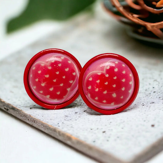 Round red stud earrings with tiny white heart pattern in a red setting displayed on a light stone surface