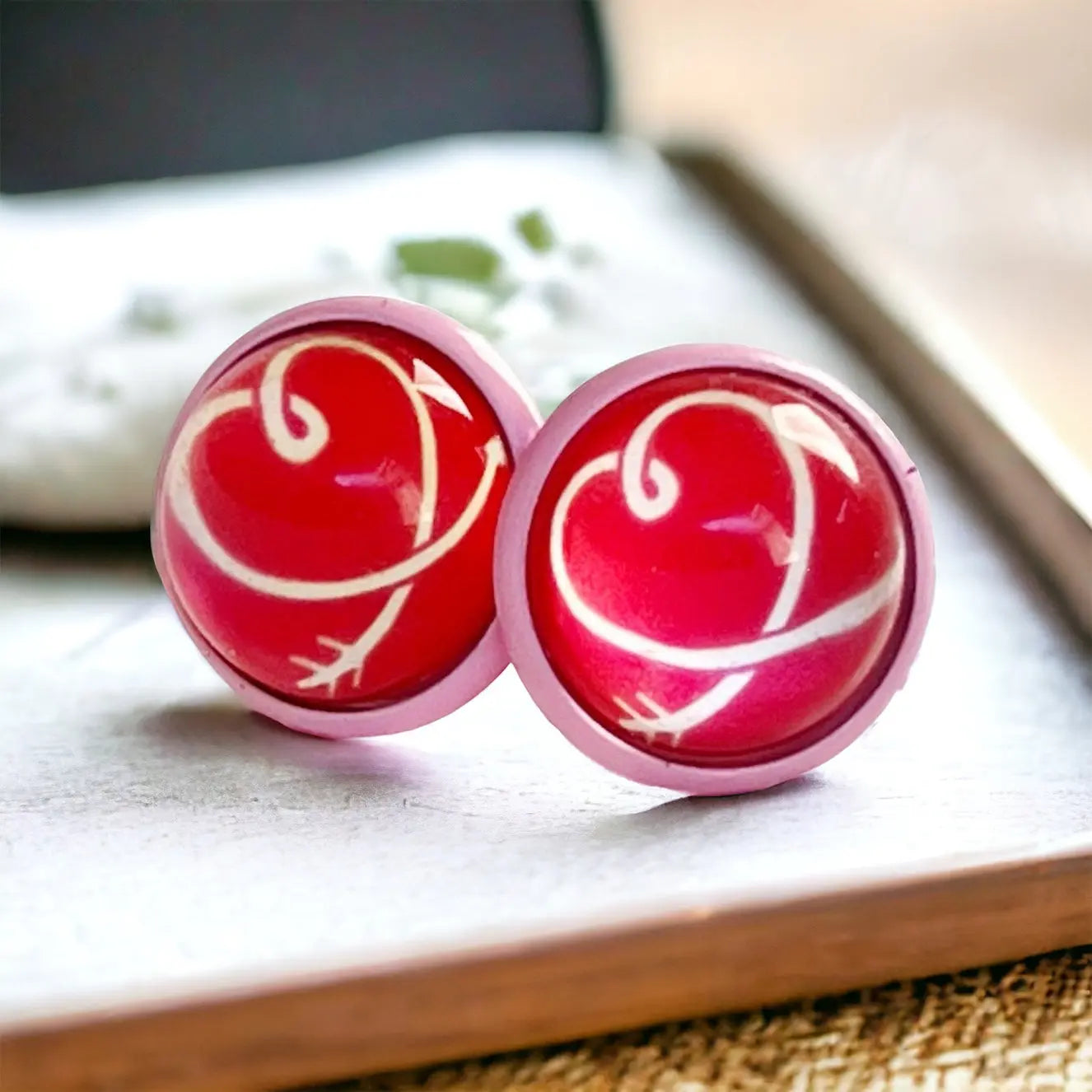 Red and pink earrings with a heart design on a wooden surface.
