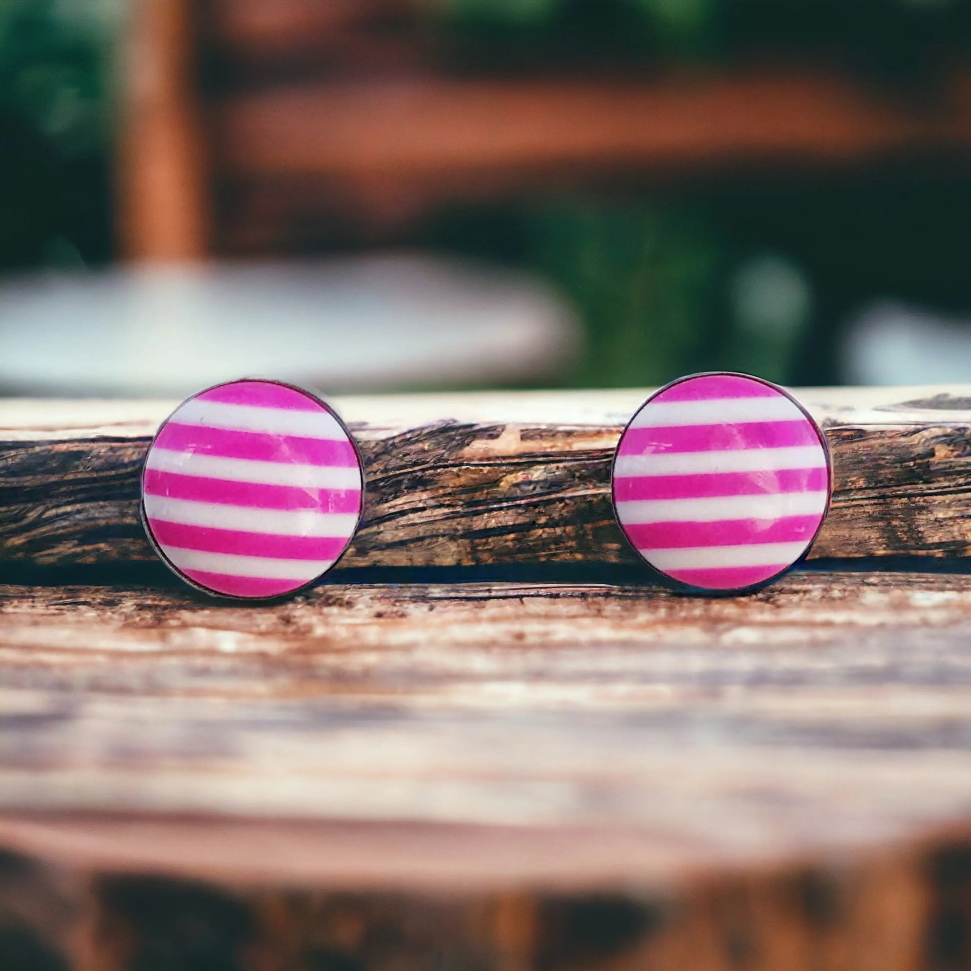 Round pink and white striped stud earrings in a silver-tone setting displayed on a rustic wood surface