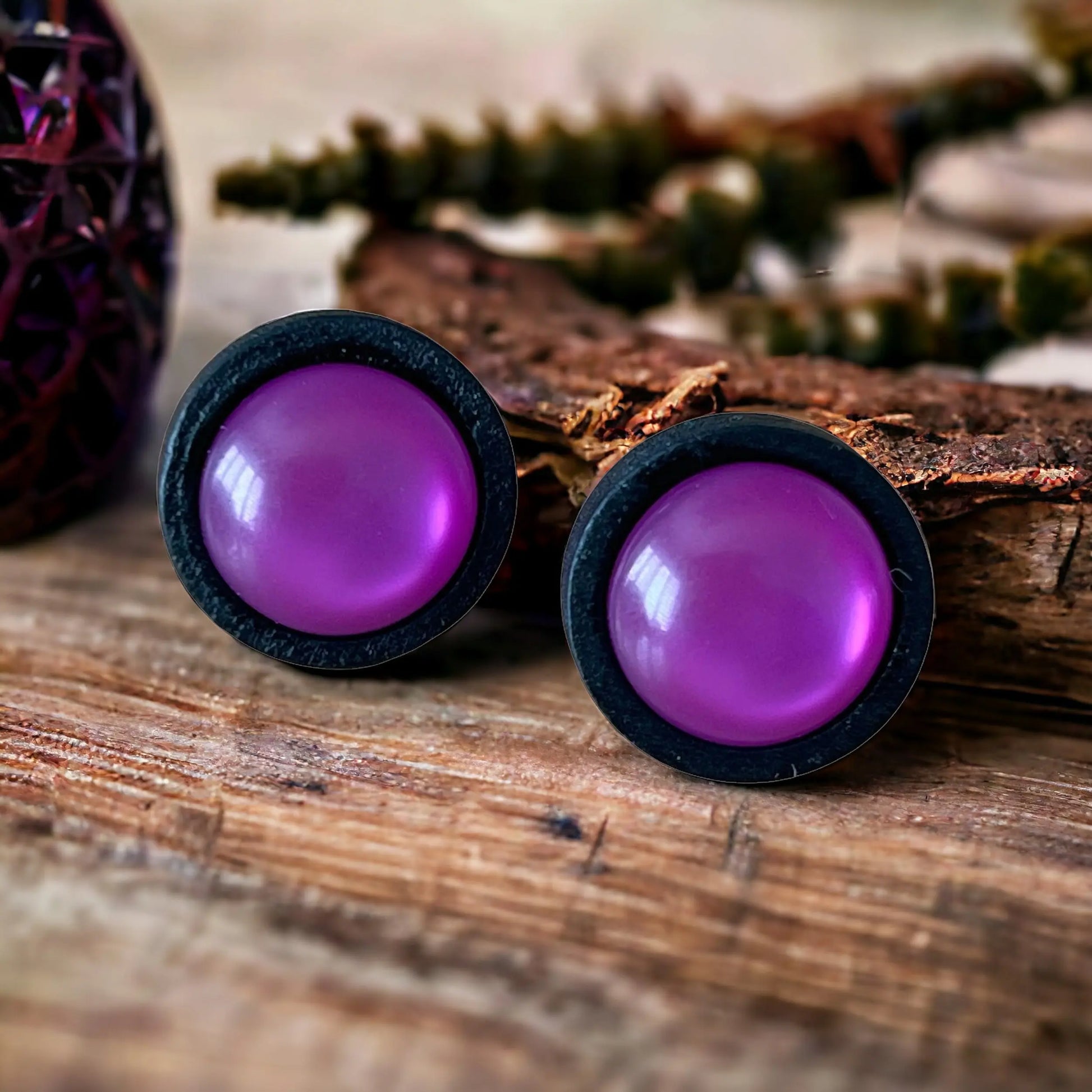 Purple round earrings with black rims on a decorative wooden surface