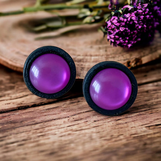 Round purple resin stud earrings with black wood border displayed on rustic wood