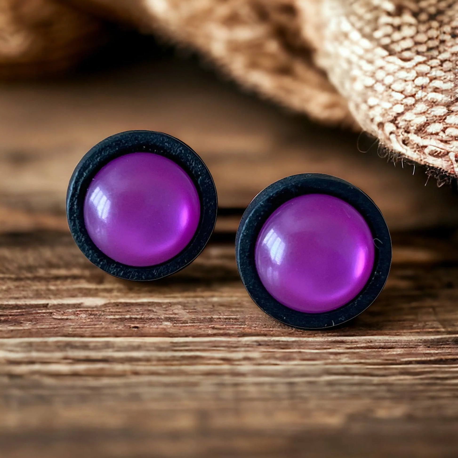 Purple round earrings with black rims on a wooden boho surface