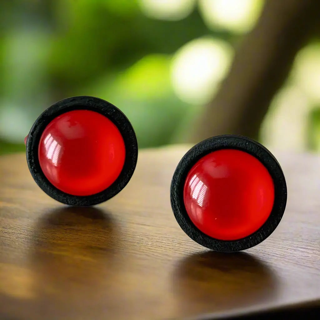 Two red earrings with black rims on a wooden surface.