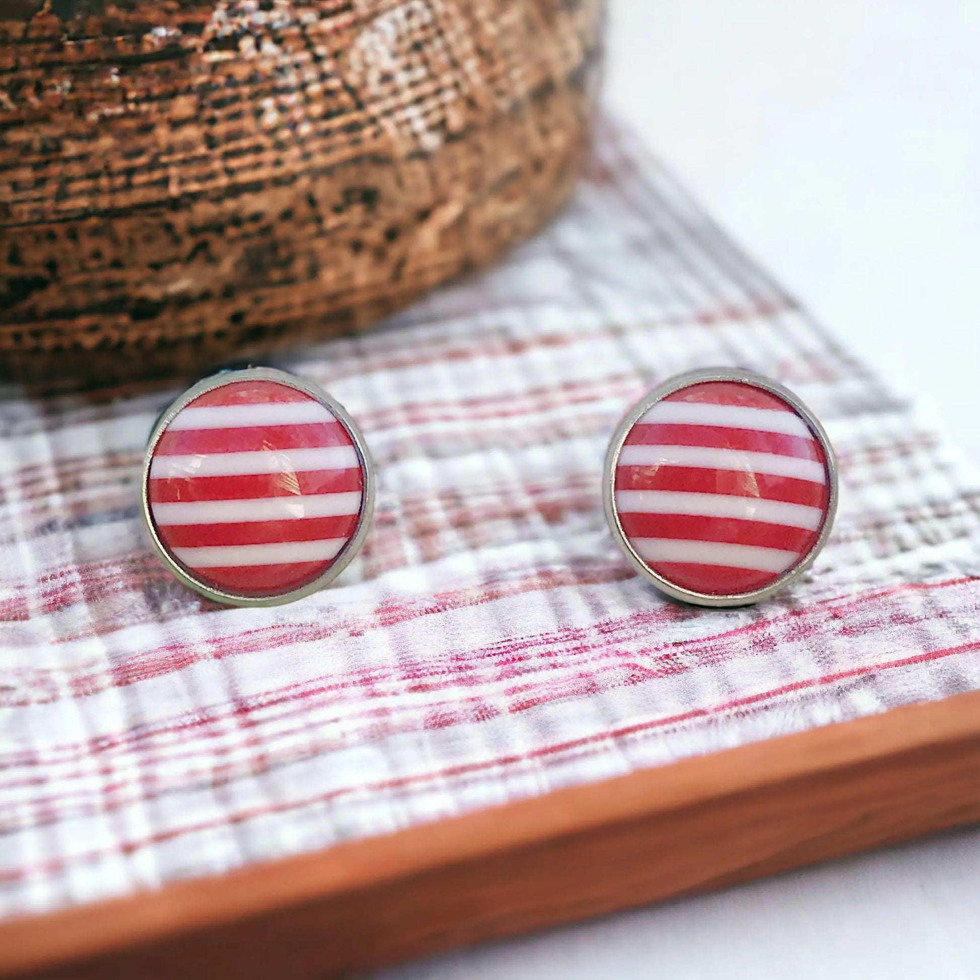 Round red and white striped stud earrings in a silver-tone setting displayed on a rustic tray