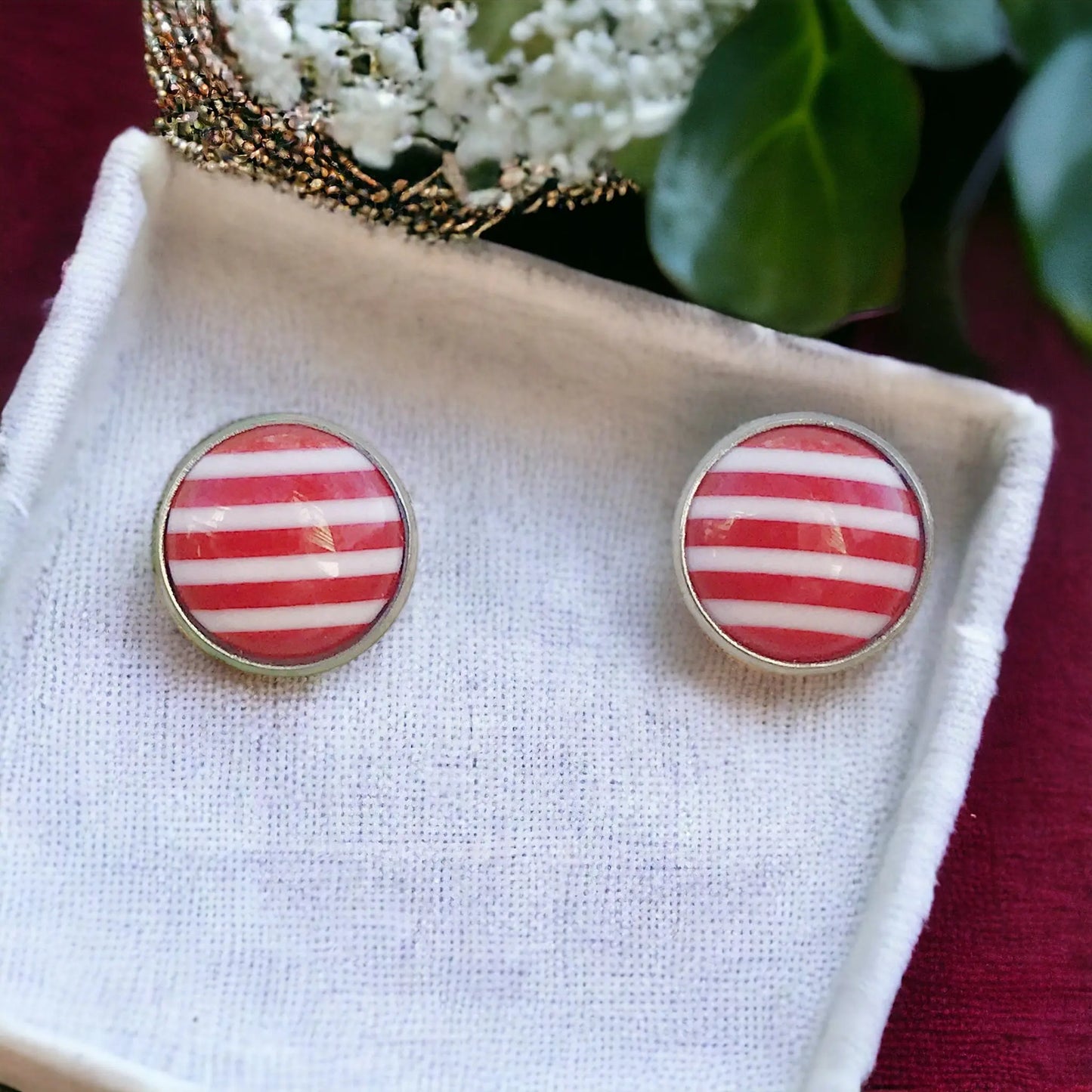 Round red and white striped stud earrings in a silver-tone setting displayed on a white tray