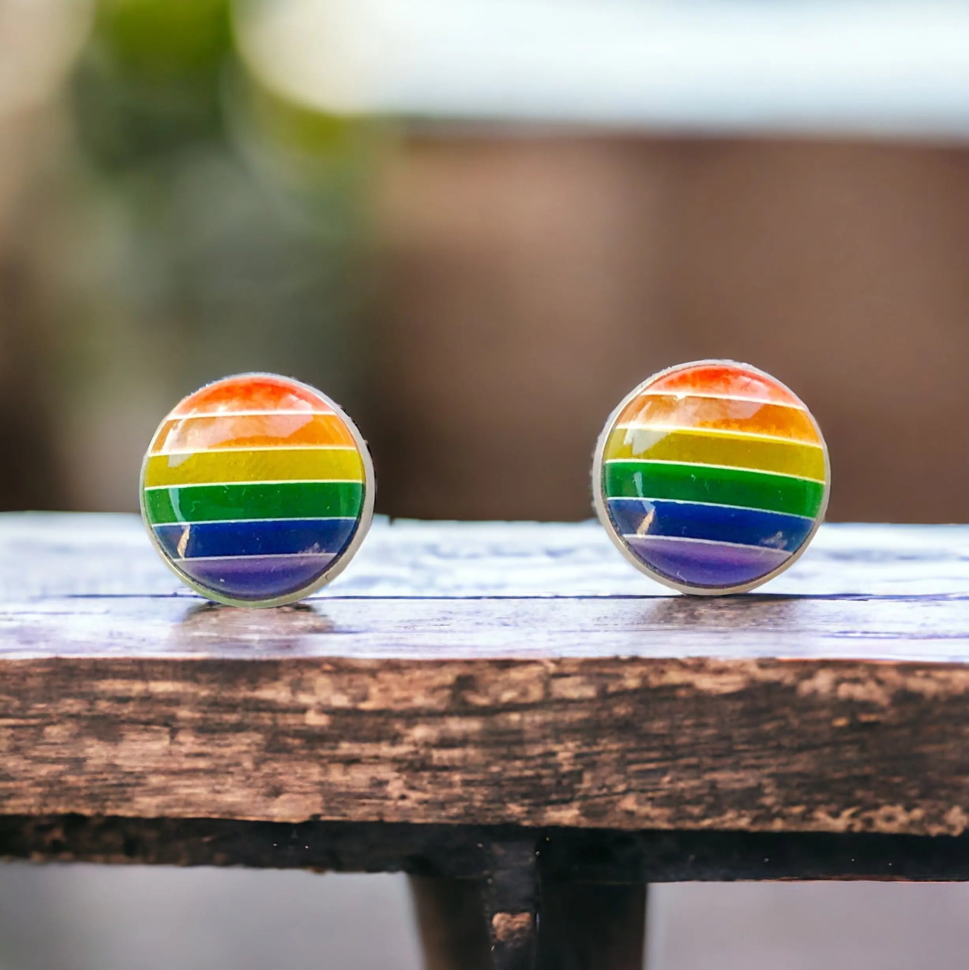 Rainbow striped earrings on a wooden surface with a blurred background