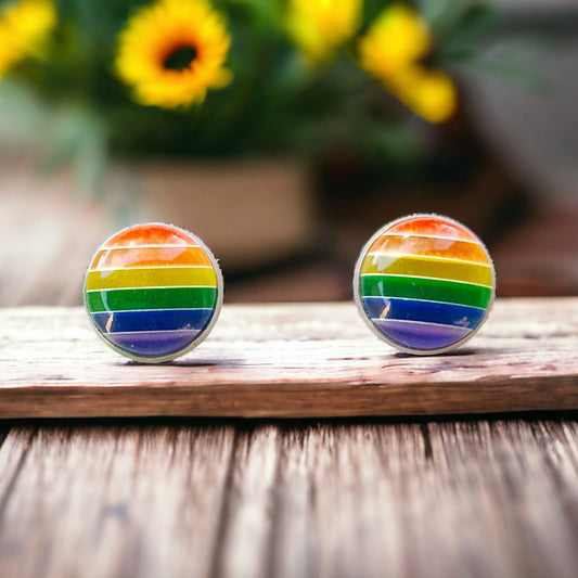 Rainbow striped earrings on a wooden surface with flowers in the background