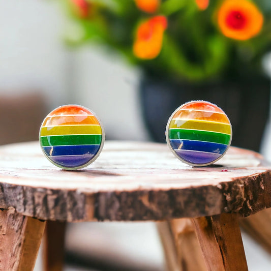 Round retro rainbow striped stud earrings in a silver-tone setting displayed on a rustic wood stool