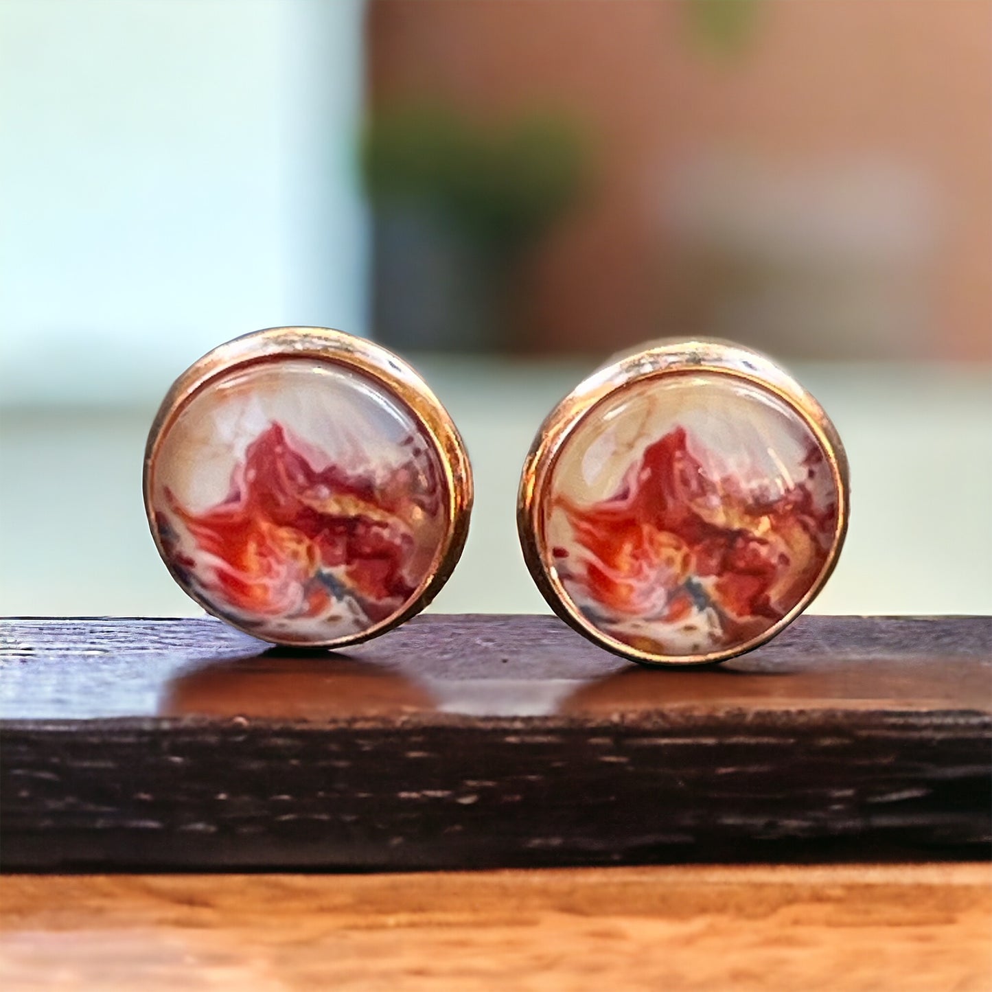 Rose gold setting stud earrings with glossy marbled resin in red, blush, and white on wooden slat