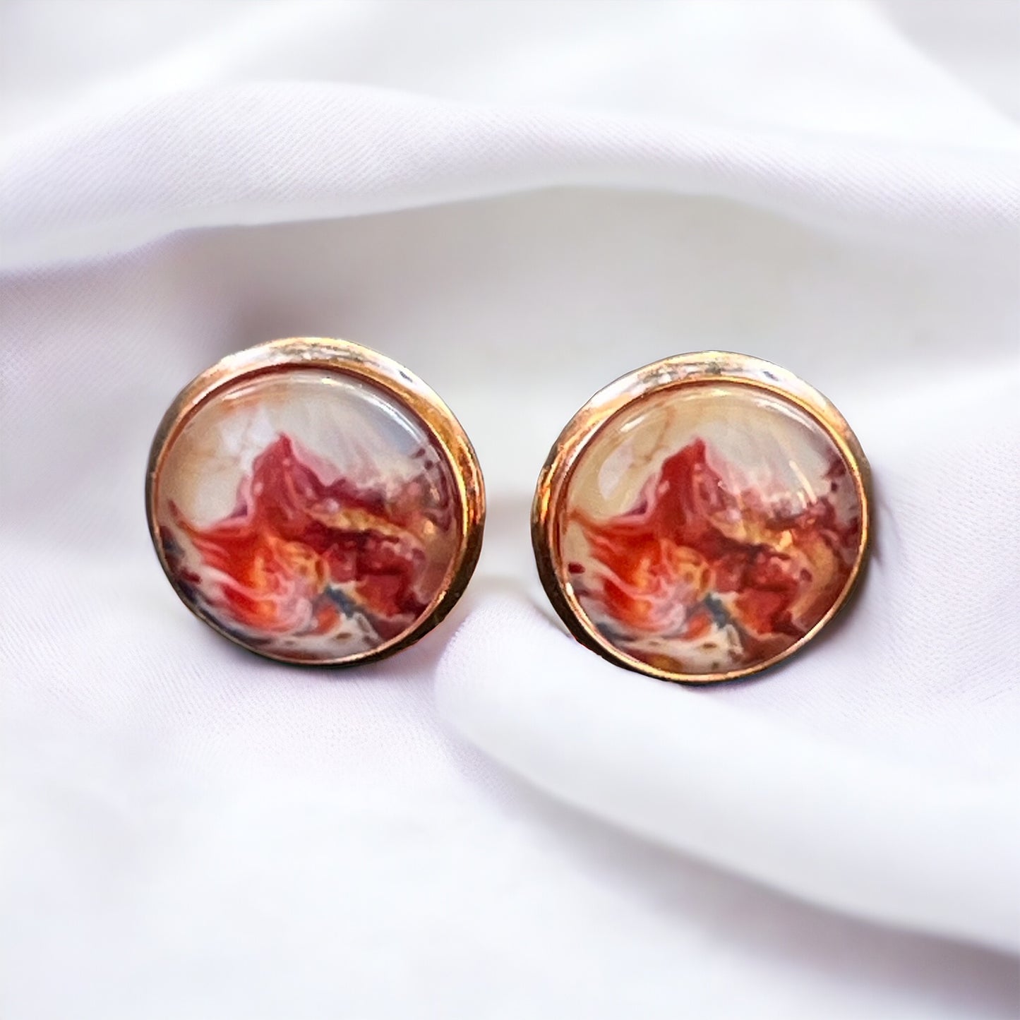 Rose gold setting stud earrings with glossy marbled resin in red, blush, and white on white material.