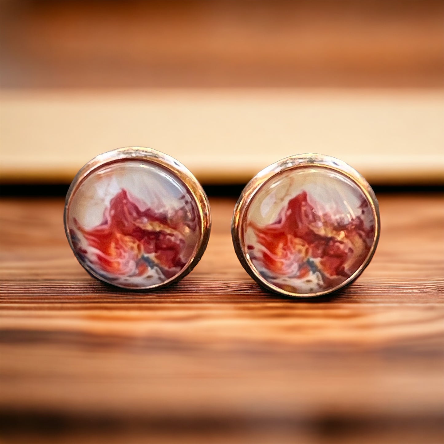 Rose gold setting stud earrings with glossy marbled resin in red, blush, and white on wood background