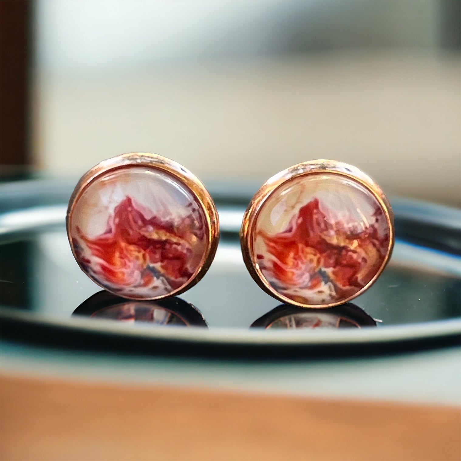 Rose gold setting stud earrings with glossy marbled resin in red, blush, and white on tray