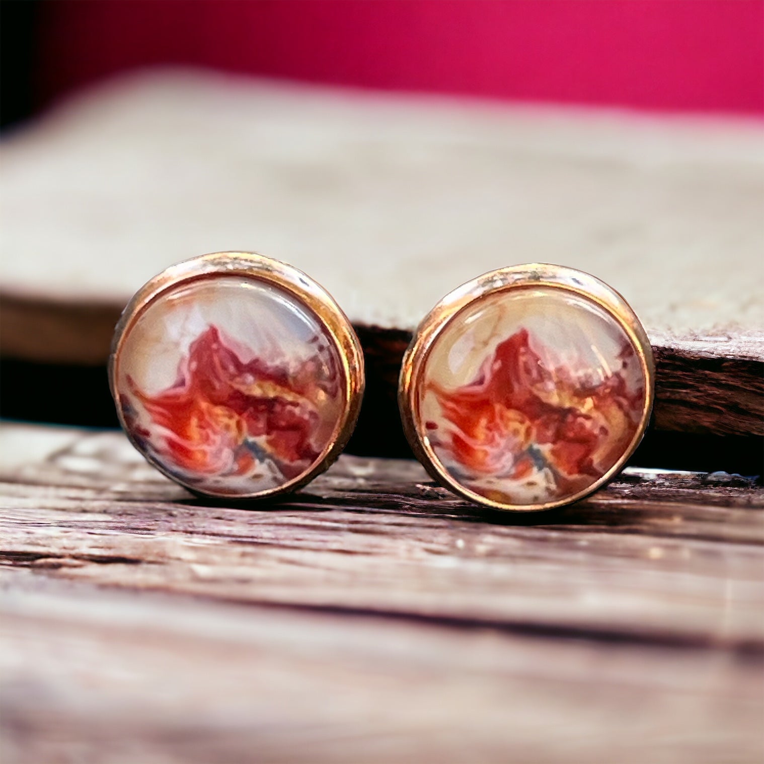 Rose gold setting stud earrings with glossy marbled resin in red, blush, and white on wood