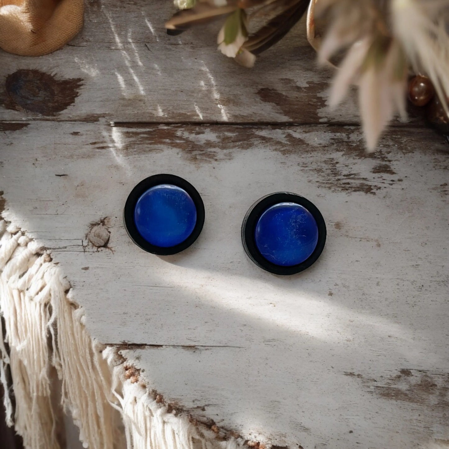 Pair of blue circular earrings on a rustic wooden surface with natural light.