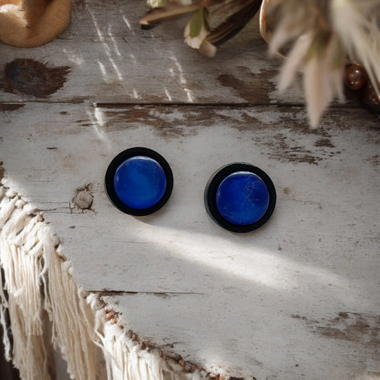 Pair of blue circular earrings on a rustic wooden surface with natural light.