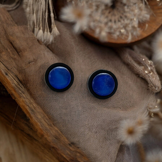 Blue circular earrings on a textured fabric background with natural elements.