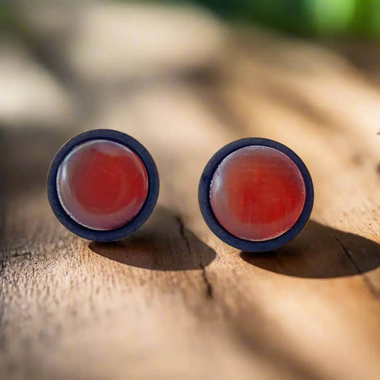 Pair of earrings with orange centers and black borders on a wooden surface