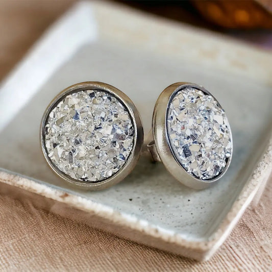 Silver druzy stud earrings on a textured white dish.