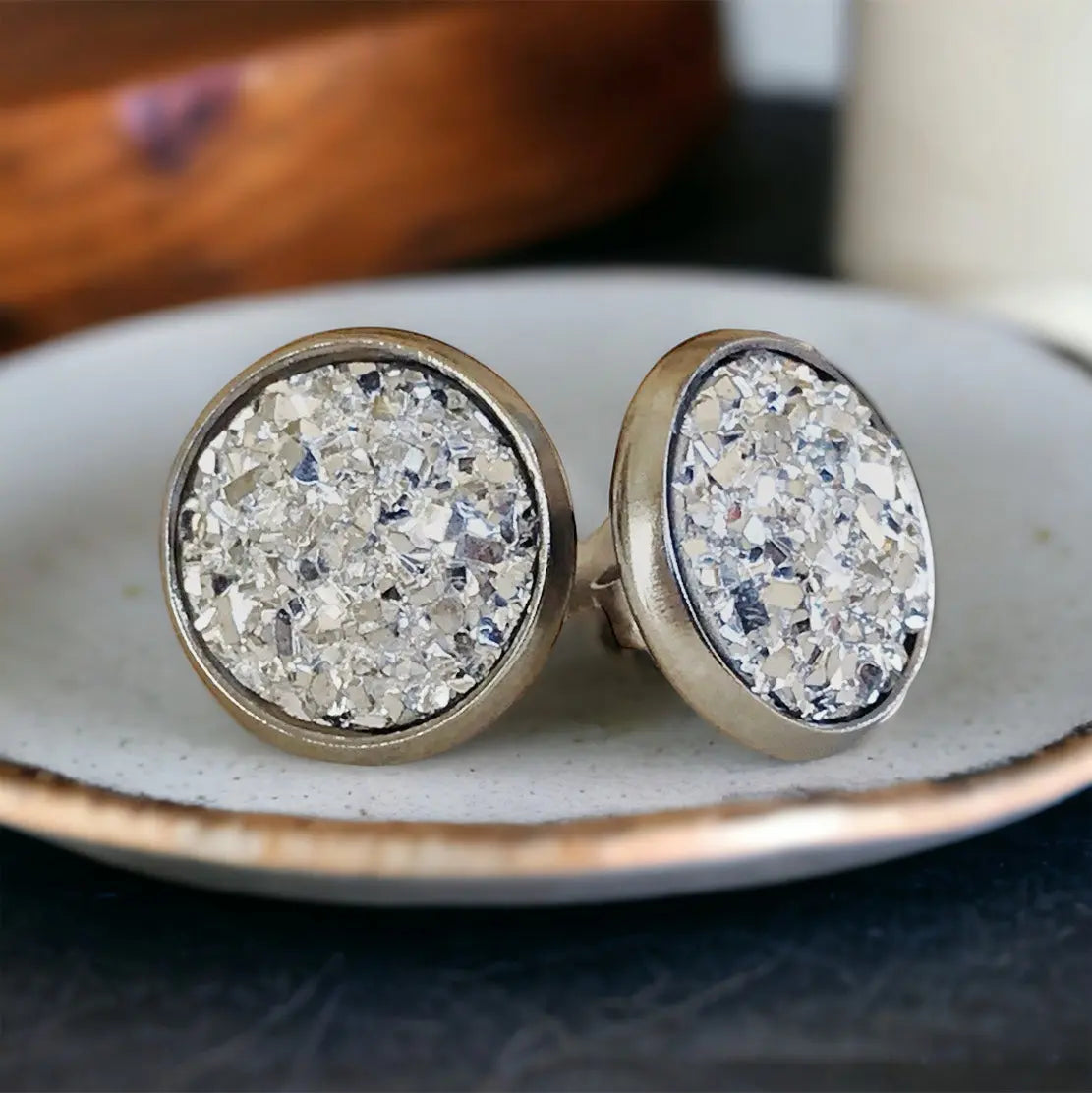 Round silver faux druzy stud earrings in a silver-tone setting displayed on a textured dish