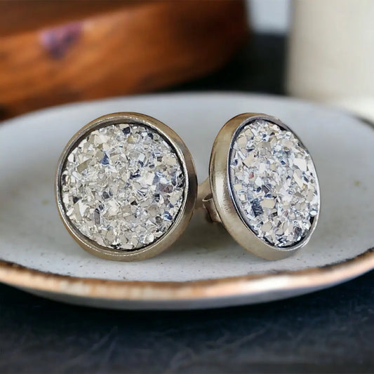 Round silver faux druzy stud earrings in a silver-tone setting displayed on a textured dish