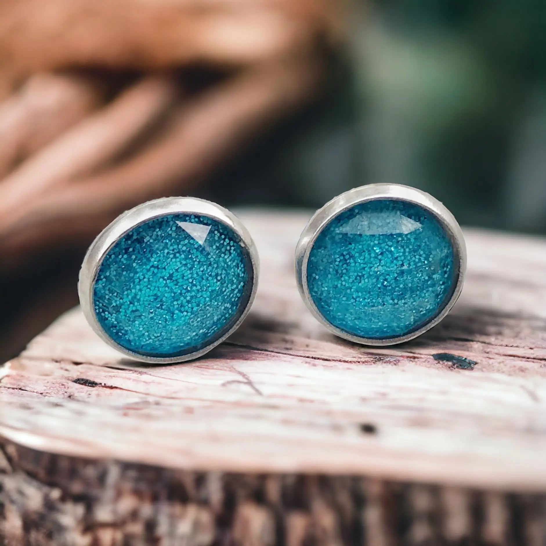 Round sky blue glitter stud earrings in a silver-tone setting displayed on a rustic wood display 