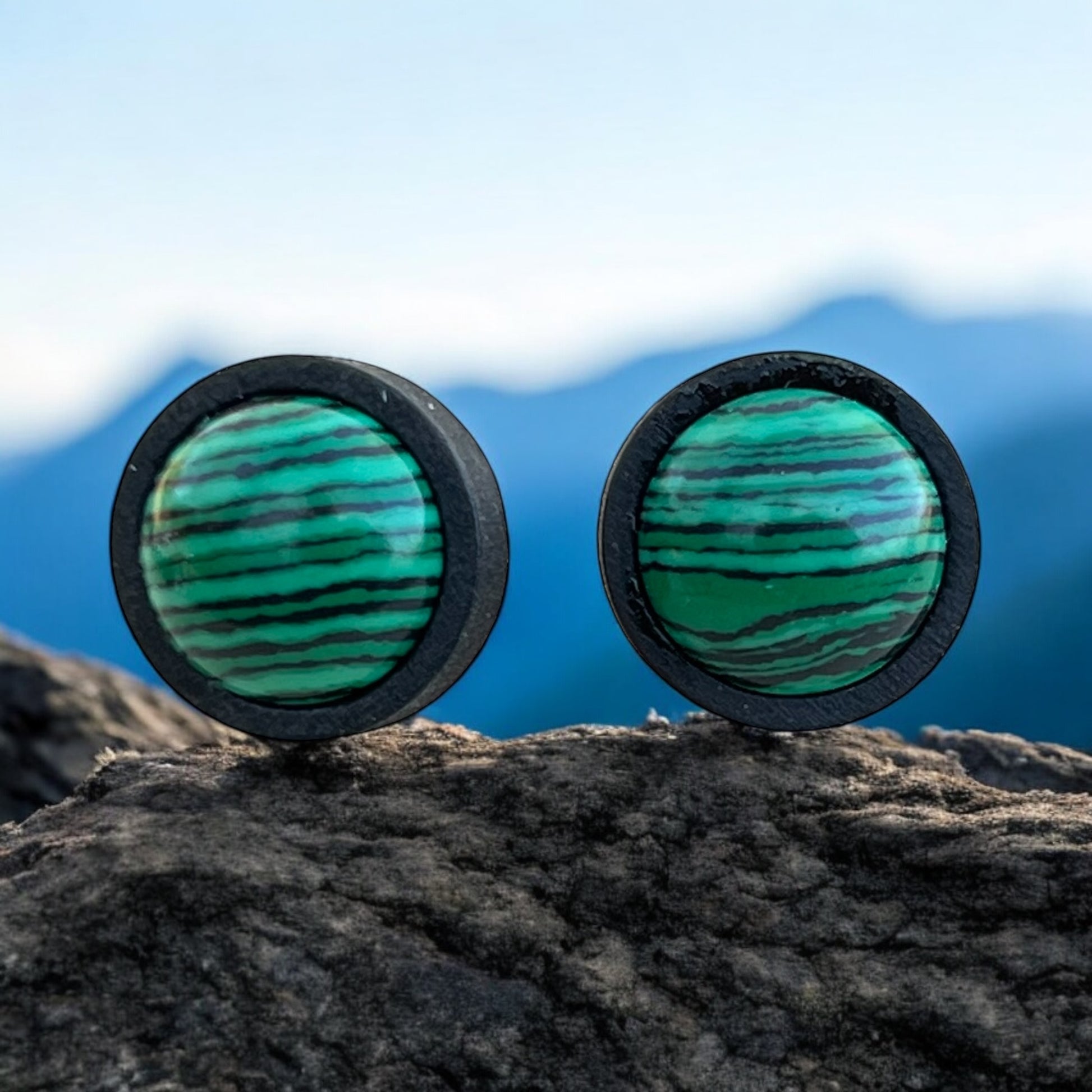 Close-up of striped green stud earrings in black wood bezel