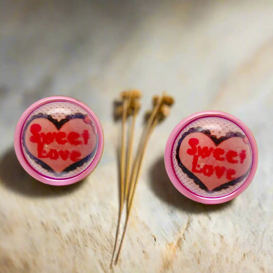 Heart-shaped earrings with 'Sweet Love' text on a textured surface.