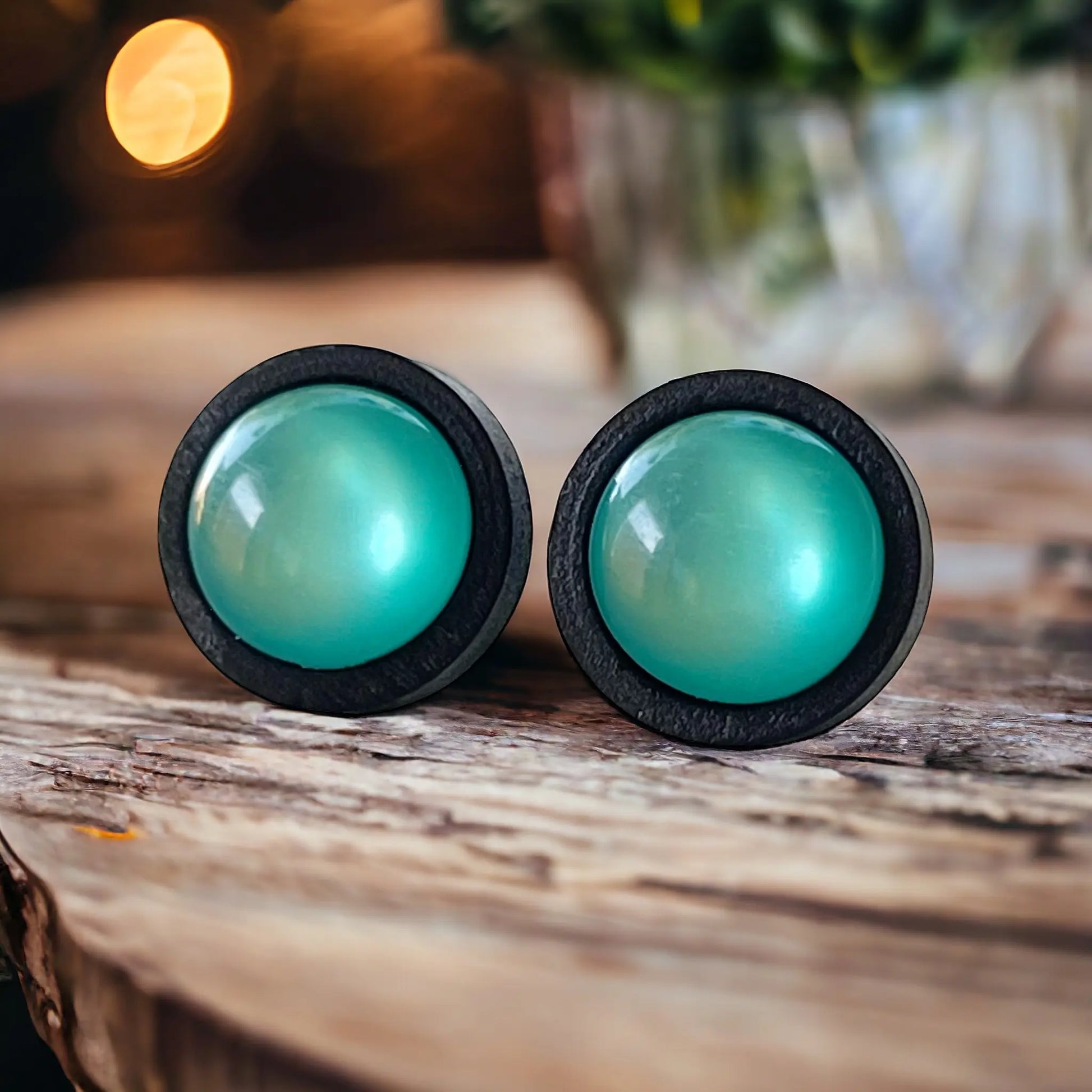 Round black wood stud earrings with glossy teal resin centers shown on wood with warm background 