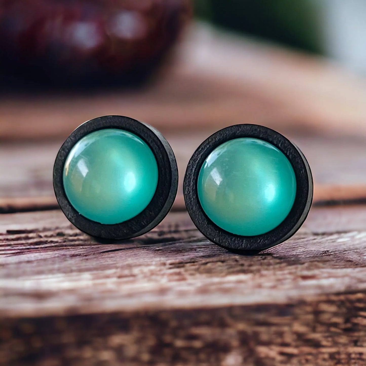 Round black wood stud earrings with glossy teal resin centers shown on wood display