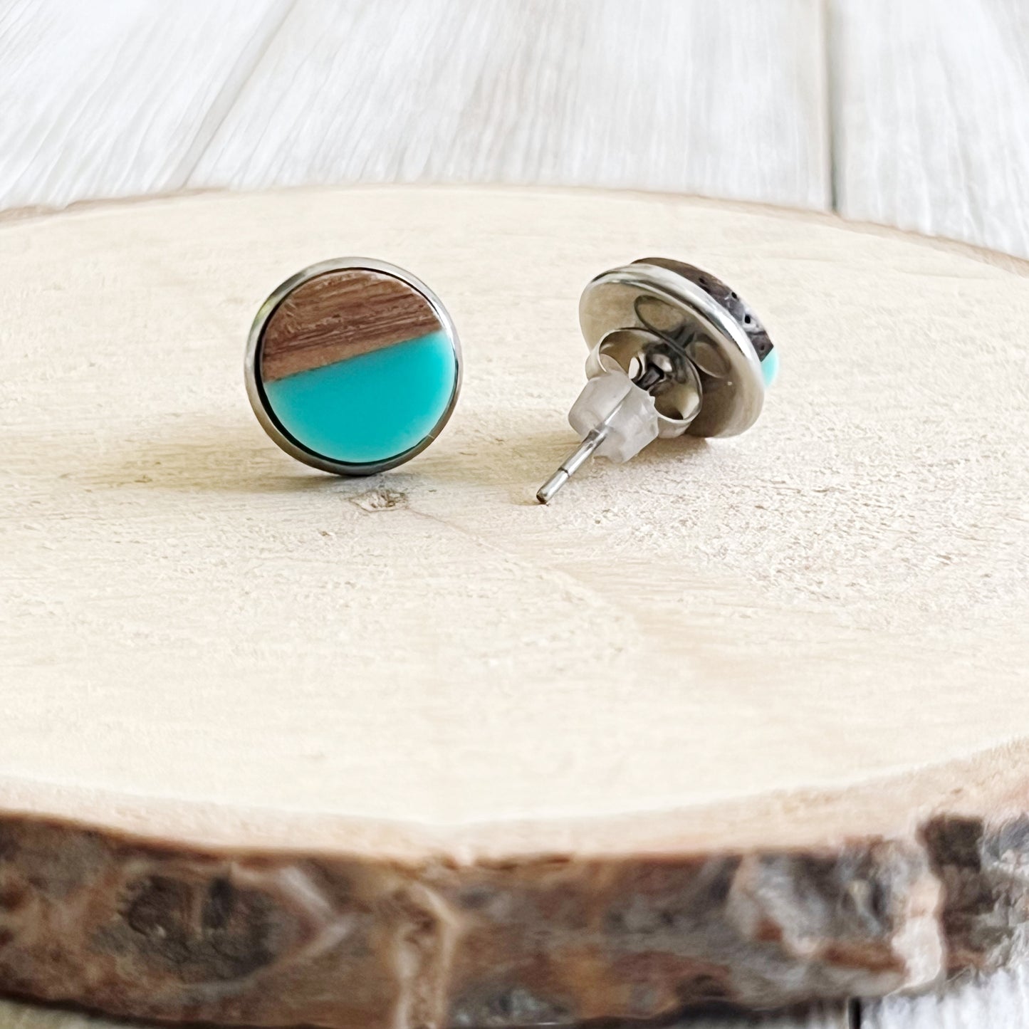 Backside of round teal and wood stud earrings with a glossy resin top displayed on a wood surface 