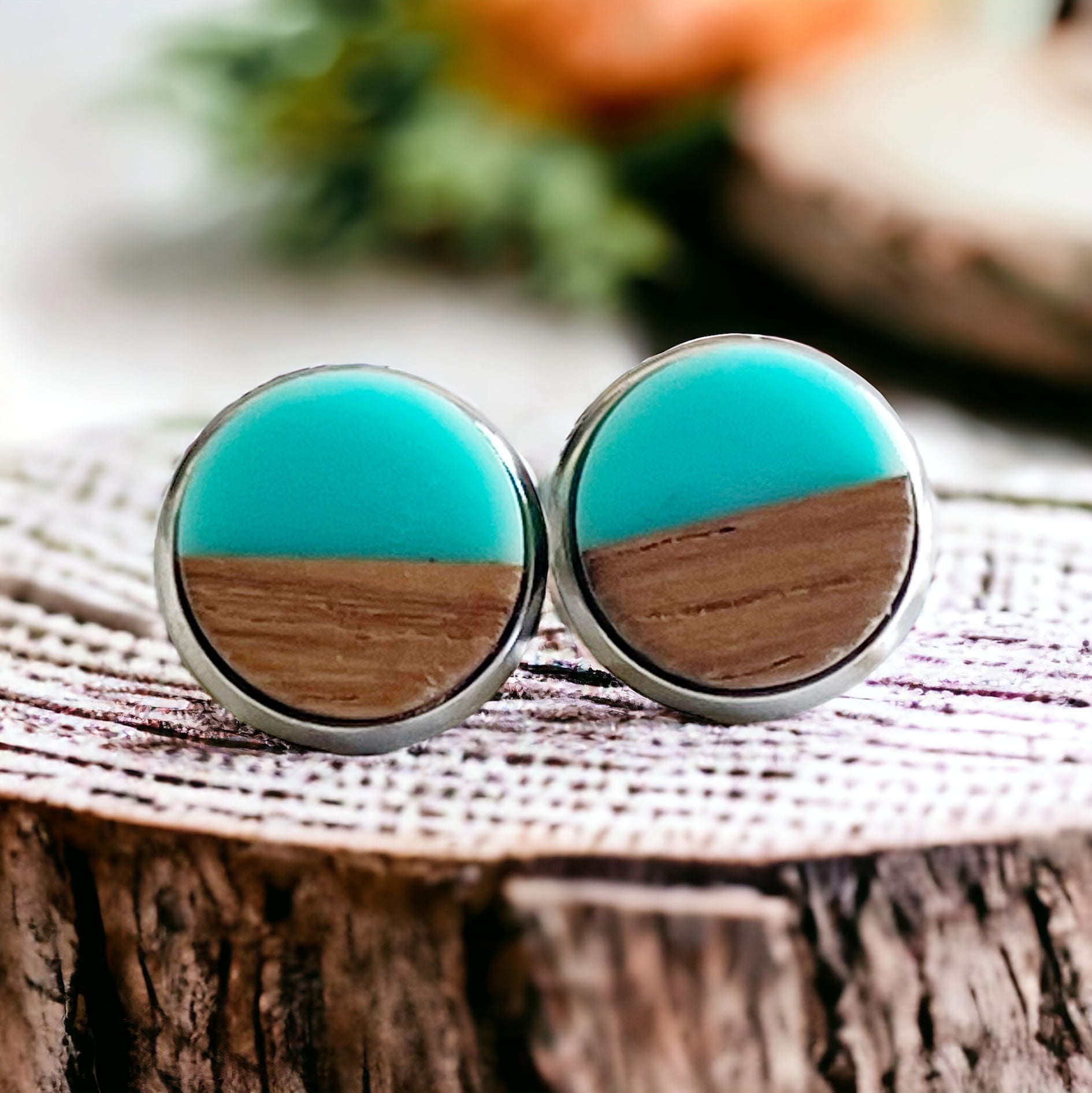 Close-up of round teal and wood stud earrings with a glossy resin top displayed on a rustic wood surface