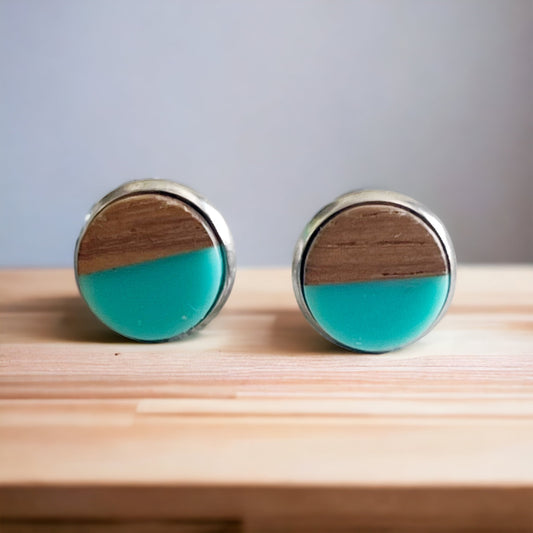 Round teal and wood stud earrings with a glossy resin top displayed on a wood surface