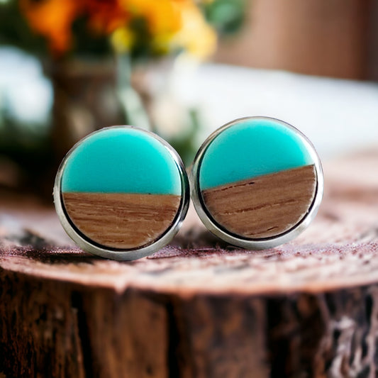 Round teal and wood stud earrings with a glossy resin top displayed on a rustic wood surface