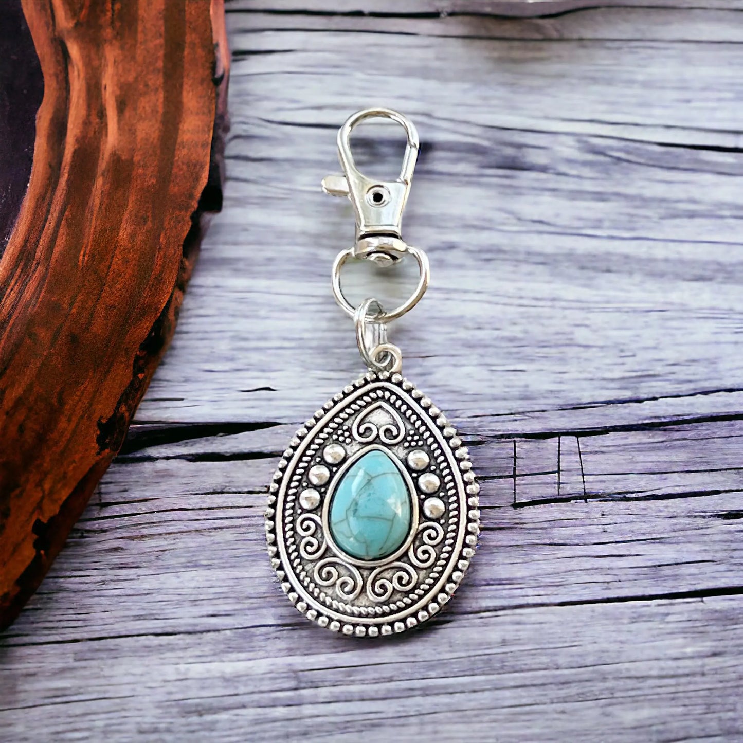 Silver purse charm with ornate medallion detail and faux turquoise accent on a styled wooden display
