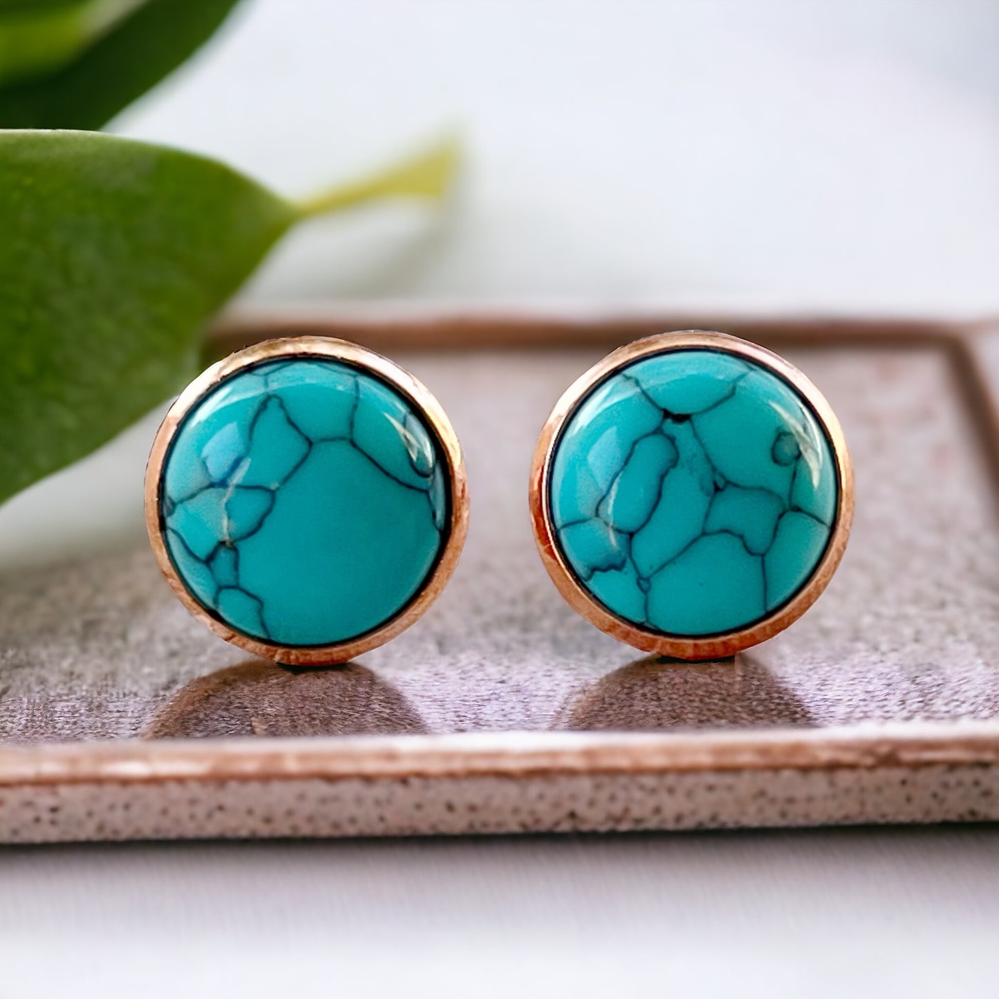 Round turquoise rose gold stud earrings displayed on a wood surface