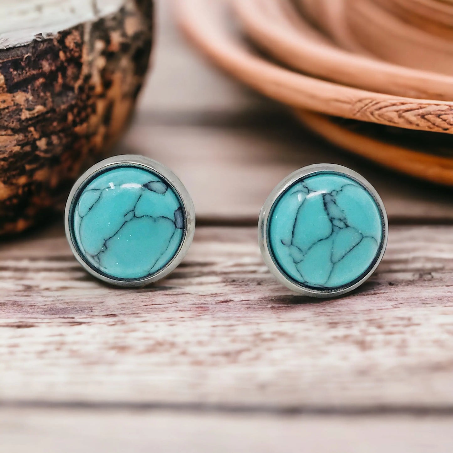 Round turquoise stud earrings in a silver-tone setting displayed on a wood surface
