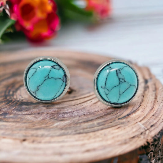 Front view of round turquoise stud earrings in a silver-tone setting displayed on a rustic wood surface