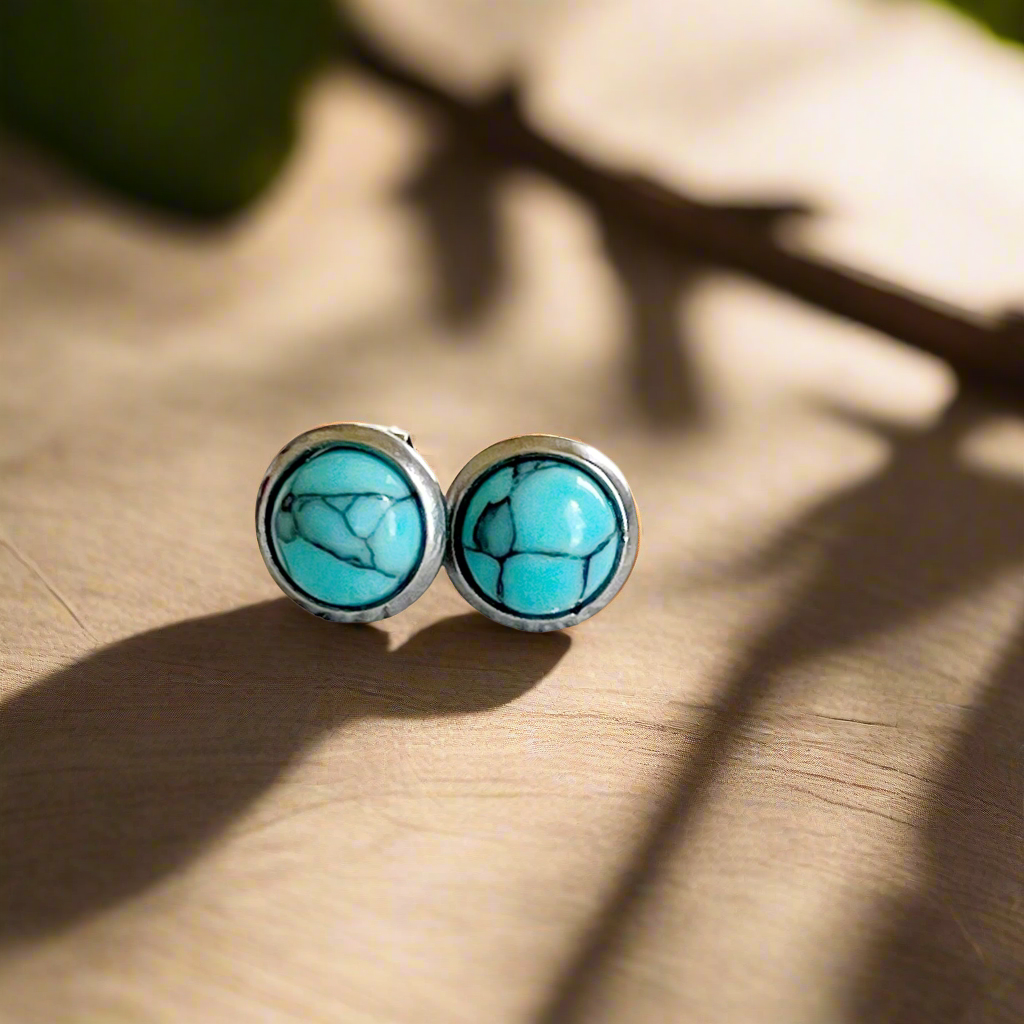 Small round turquoise stud earrings in a silver-tone setting on wood display 